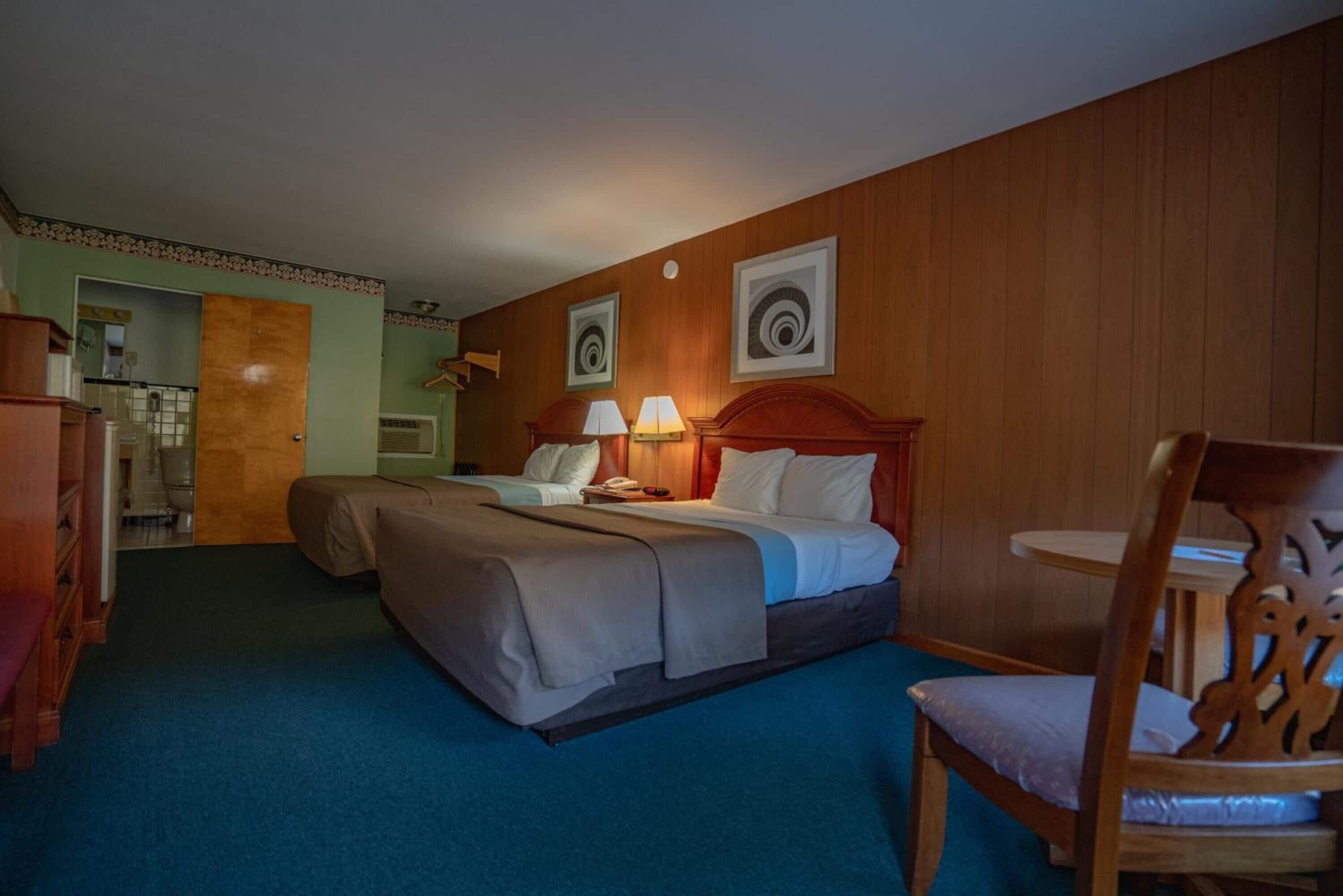 Ein Hotelzimmer mit einem Bett, zwei Nachttischen mit Lampen, einem Holzstuhl und einem kleinen Tisch.