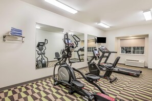 Une salle de sport équipée de vélos d’appartement, de tapis de course et d’un mur recouvert de miroirs.