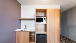 A compact kitchenette with a microwave, sink, and built-in refrigerator.