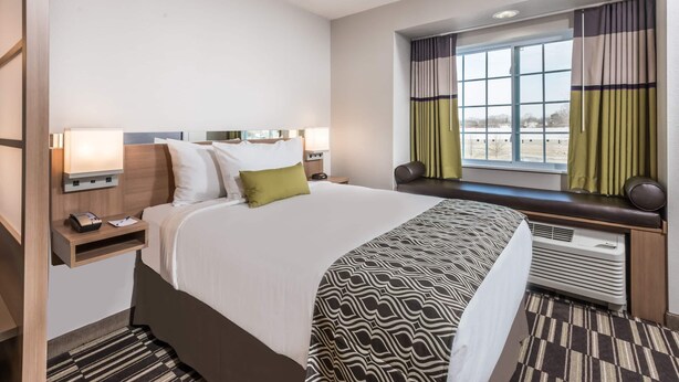 A hotel room with a large bed, bedside tables, a window with curtains, and a built-in heater.