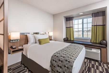 A hotel room with a large bed, bedside tables, a window with curtains, and a built-in heater.