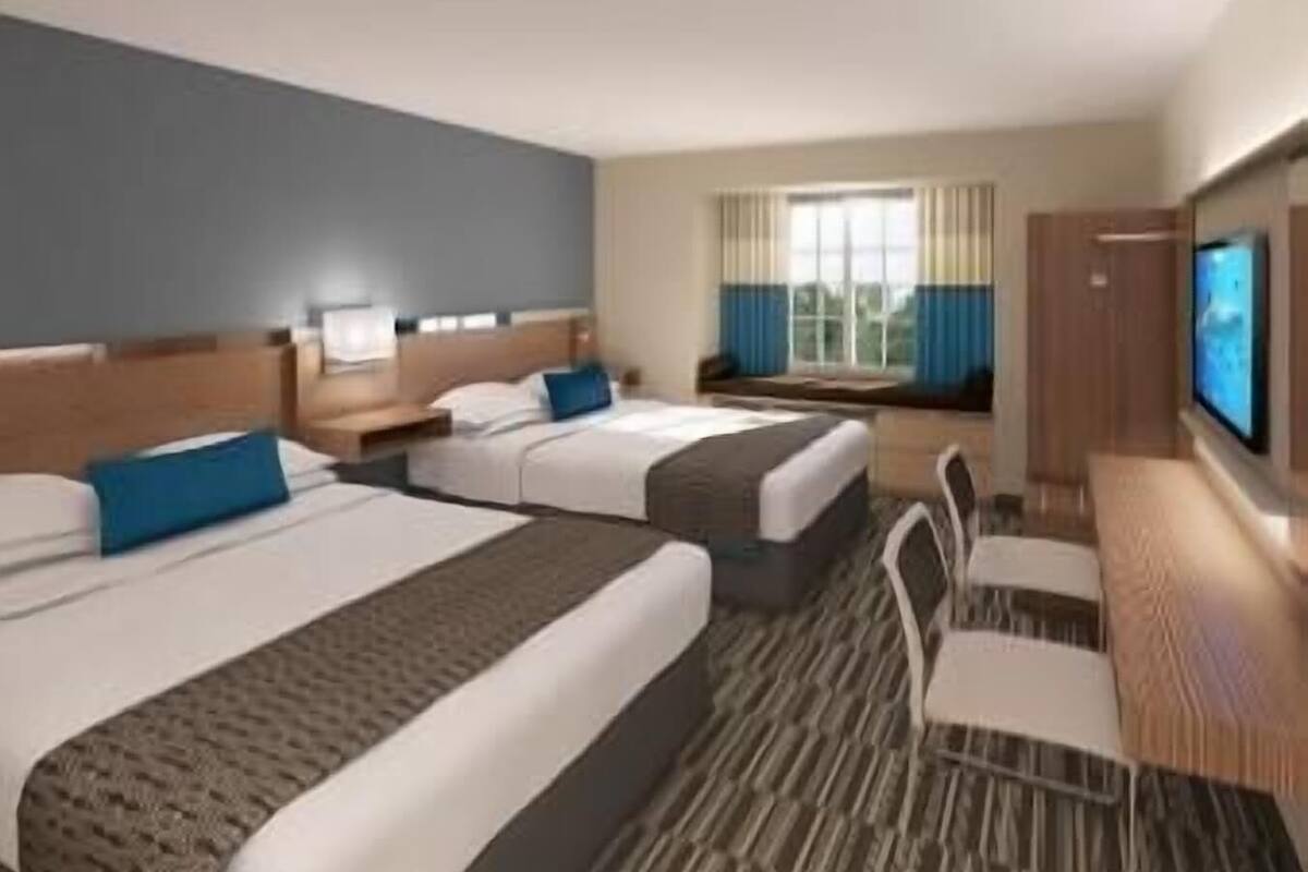 A hotel room with two beds, a desk, a chair, a TV, and a window with curtains.