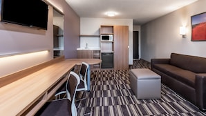 A compact hotel room with a kitchenette, a flat-screen TV, a sofa, and a small dining table.