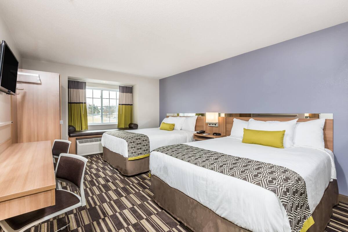 A hotel room with two beds, a desk, and a TV.