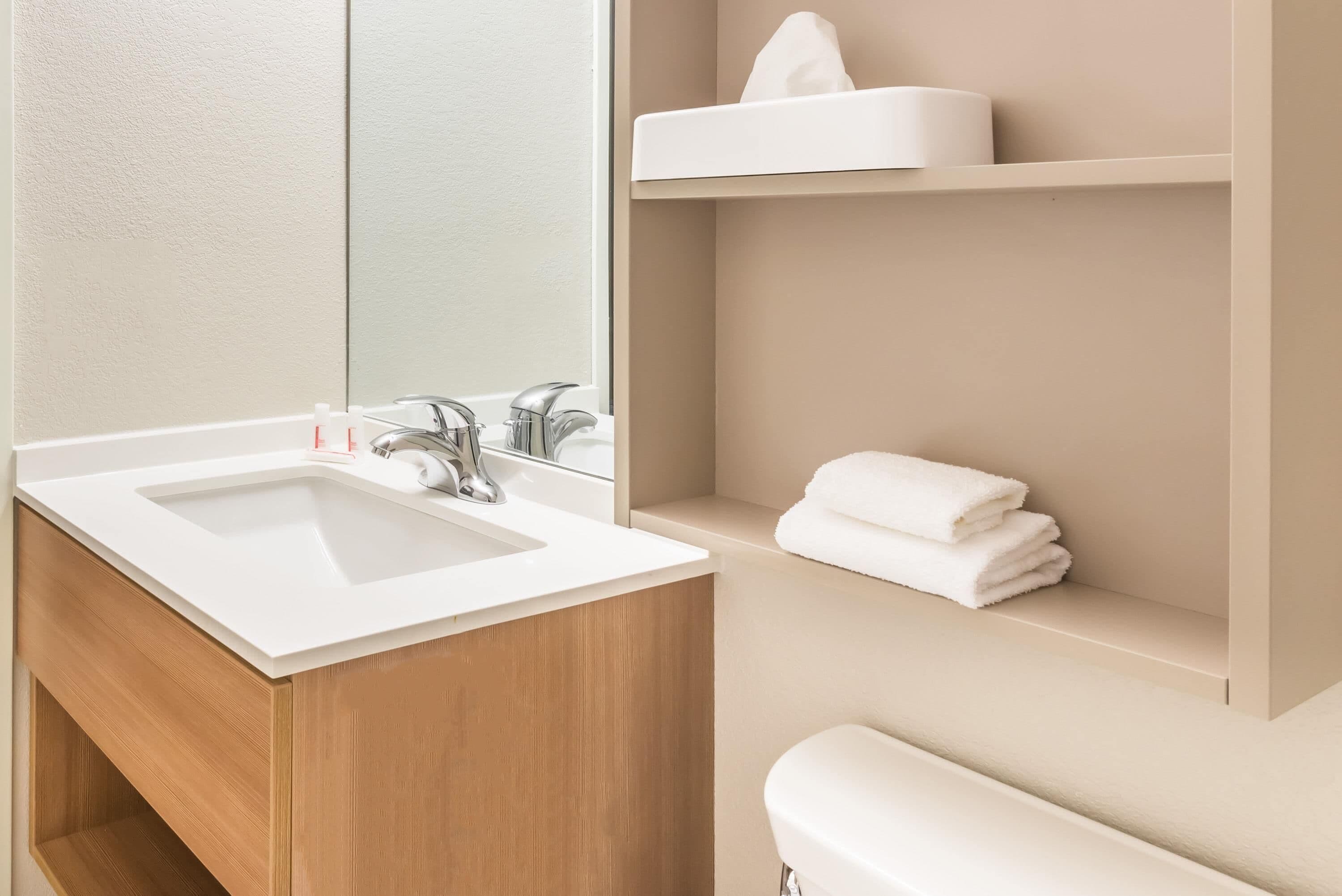 A modern bathroom with a white sink, wooden vanity, and a mirror.