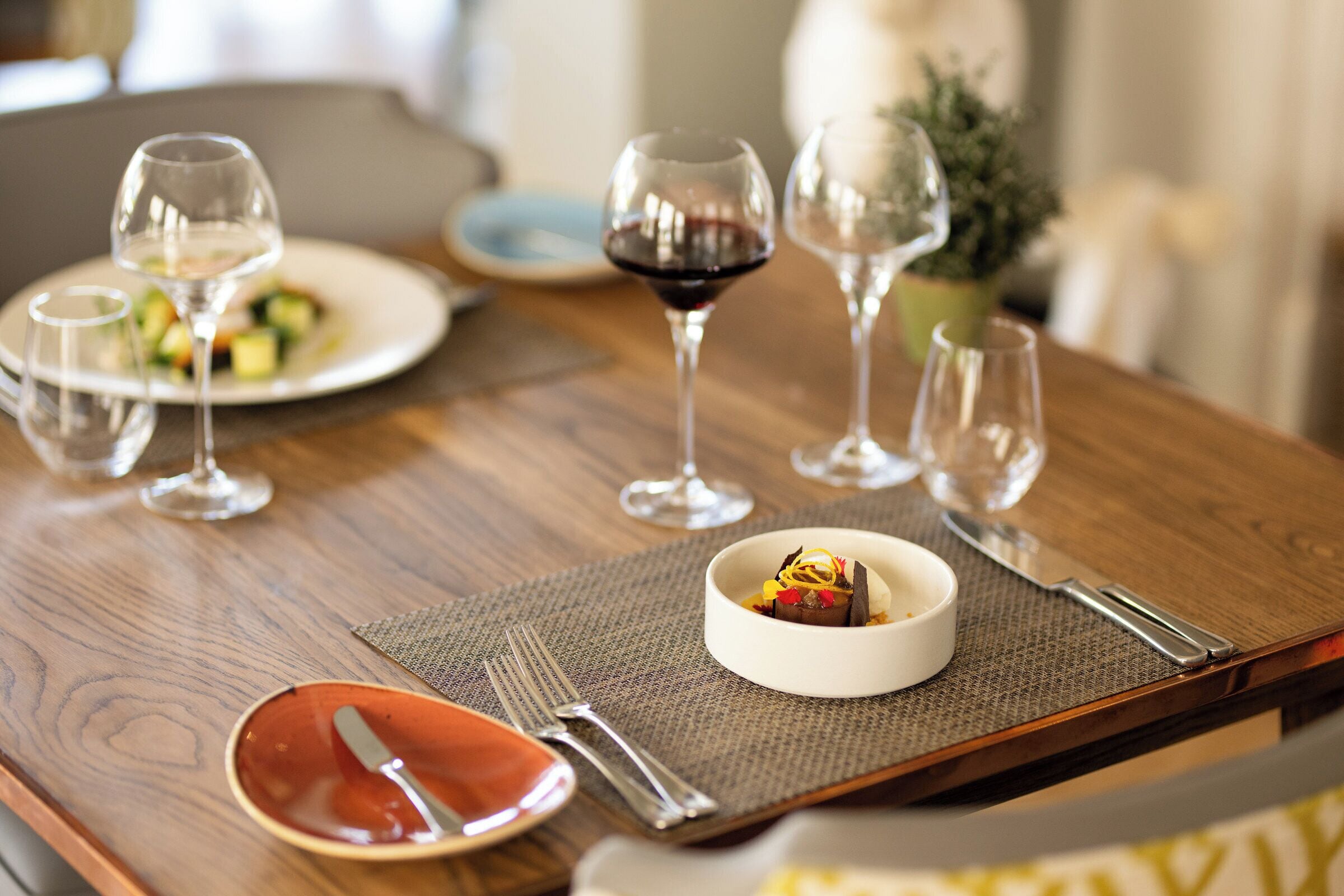 A dining table with a white bowl of dessert, wine glasses, and cutlery.