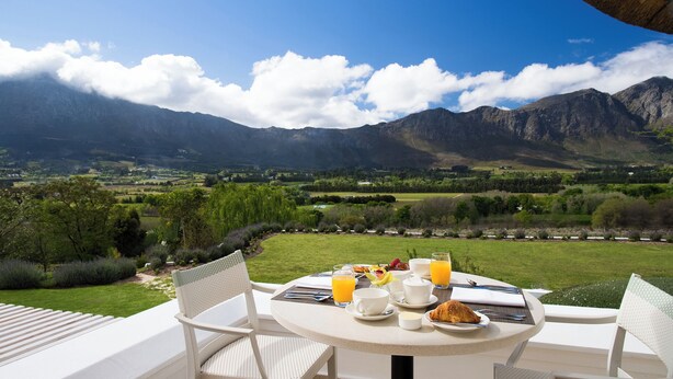 A table set for breakfast with a mountain view, white chairs, and a table umbrella. - Mont Rochelle Hotel & Vineyard (Franschhoek)