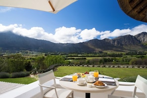 A table set for breakfast with a mountain view, white chairs, and a table umbrella. - Mont Rochelle Hotel & Vineyard (Franschhoek)