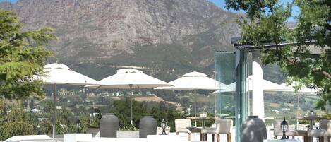 Une terrasse avec des sièges extérieurs, des parasols blancs et une vue sur les montagnes en arrière-plan.