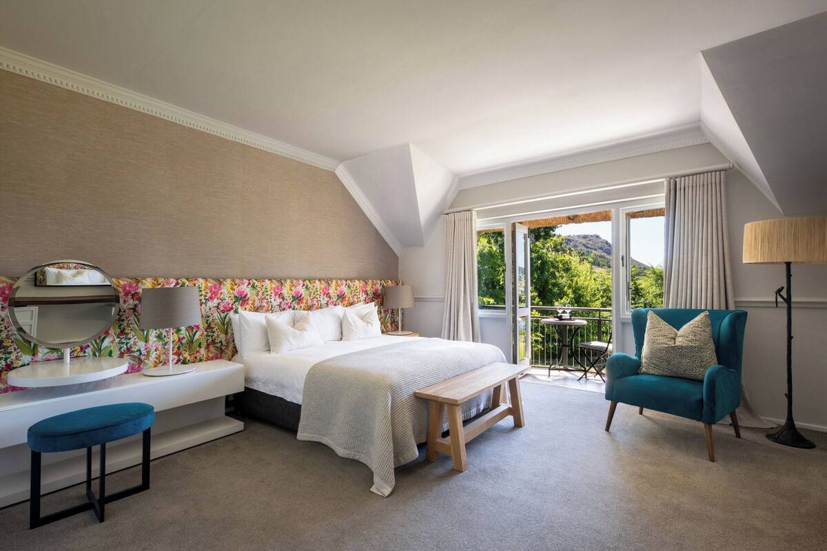 A bedroom with a bed, a bedside table, a chair, and a view of the outdoors.