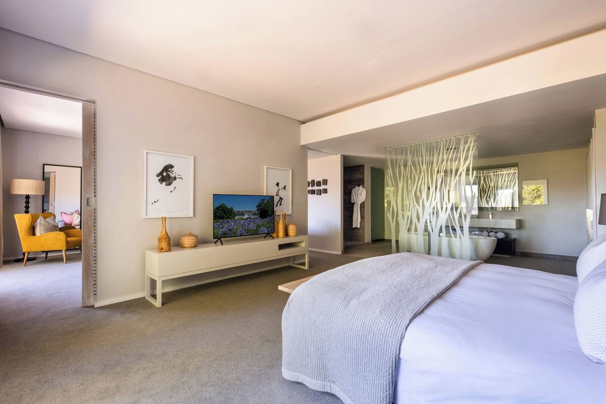 A modern hotel room with a large bed, a TV, a sofa, and a bathroom visible through an open door.
