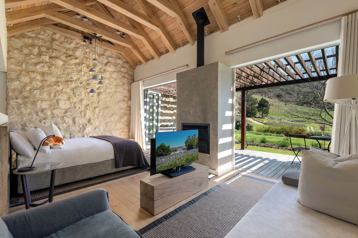 Une chambre avec un mur en pierre, un lit, une télévision et une vue sur un jardin.