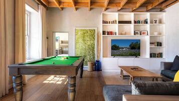 A room with a pool table, a sofa, a television, and bookshelves.