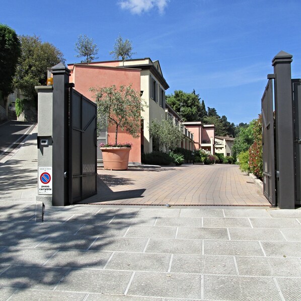 A gated entrance to a residential area with a paved driveway, a no parking sign, and a potted plant.