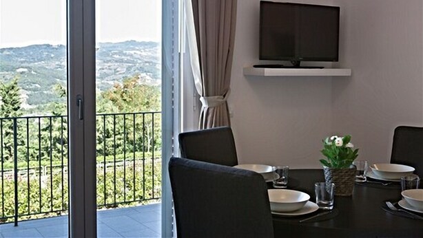 A dining area with a table set for four, a flat-screen TV mounted on the wall, and a view of a mountainous landscape through a sliding glass door.