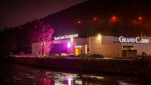 A Grand Casino building with illuminated signage, a waterfront view, and a parking area. - Western City (Chaudfontaine)