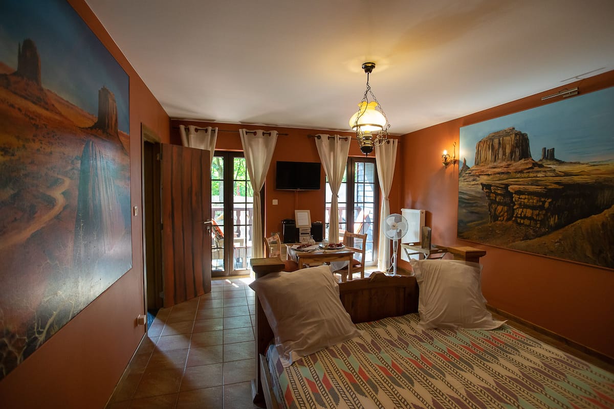A hotel room with a bed, a desk, a chair, a television, and a painting on the wall.