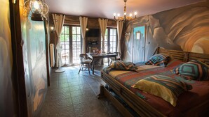 A bedroom with a bed, a desk, and a chair. There are curtains on the windows, and a chandelier hangs from the ceiling. - Western City (Chaudfontaine)