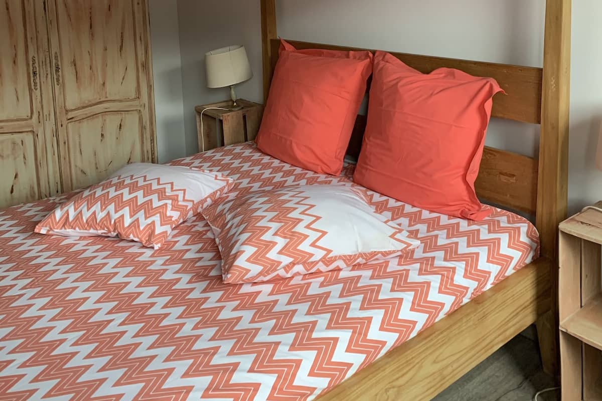 A bed with a chevron-patterned bedspread, two red pillows, and a sheer canopy.