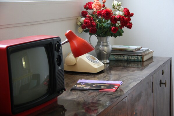 A vintage red television, a red desk lamp, a vase with red and white flowers, and some books on a wooden desk. - Miguel Torga Vintage Lofts (Coimbra)