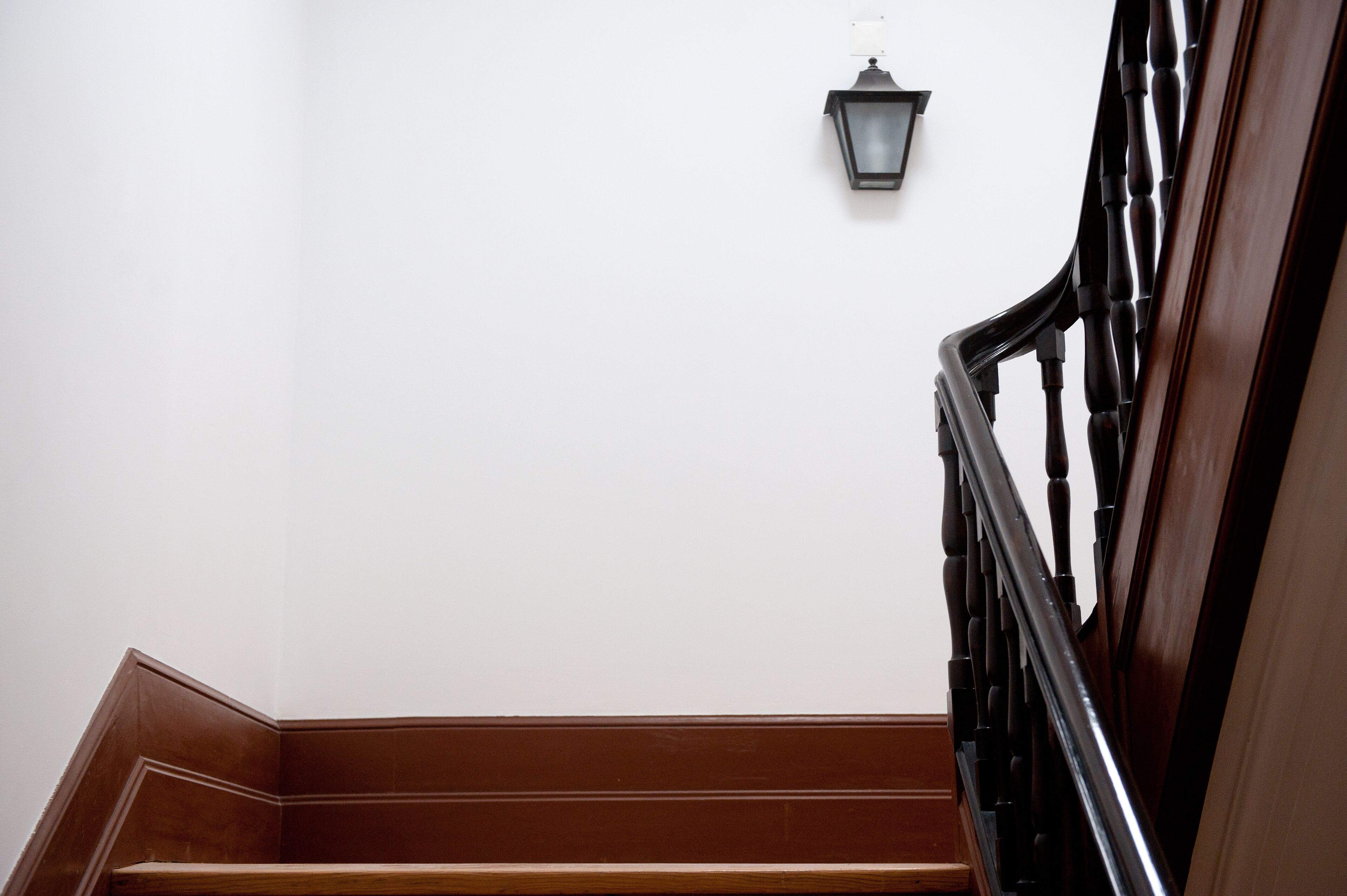 Una escalera de madera con barandilla negra y una lámpara de pared.