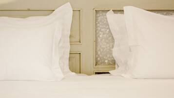 A bed with white linens and a window with frosted glass.