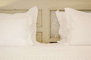 A bed with white linens and a window with frosted glass.