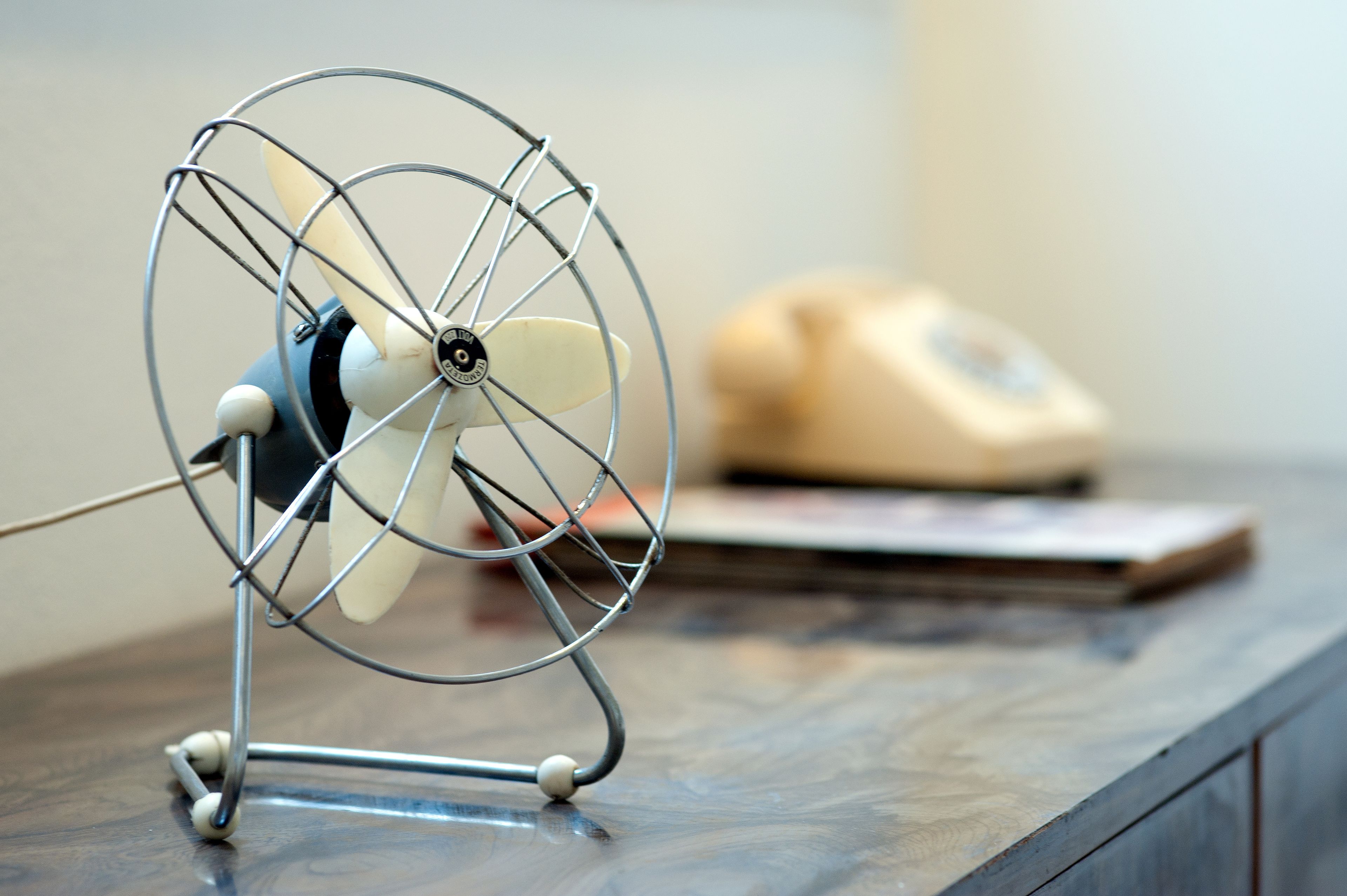 A small fan on a wooden surface with a telephone and a book in the background.