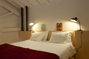 A neatly made bed with white linens and a red blanket, two wall-mounted lamps, and artwork on the wall. - Miguel Torga Vintage Lofts (Coimbra)