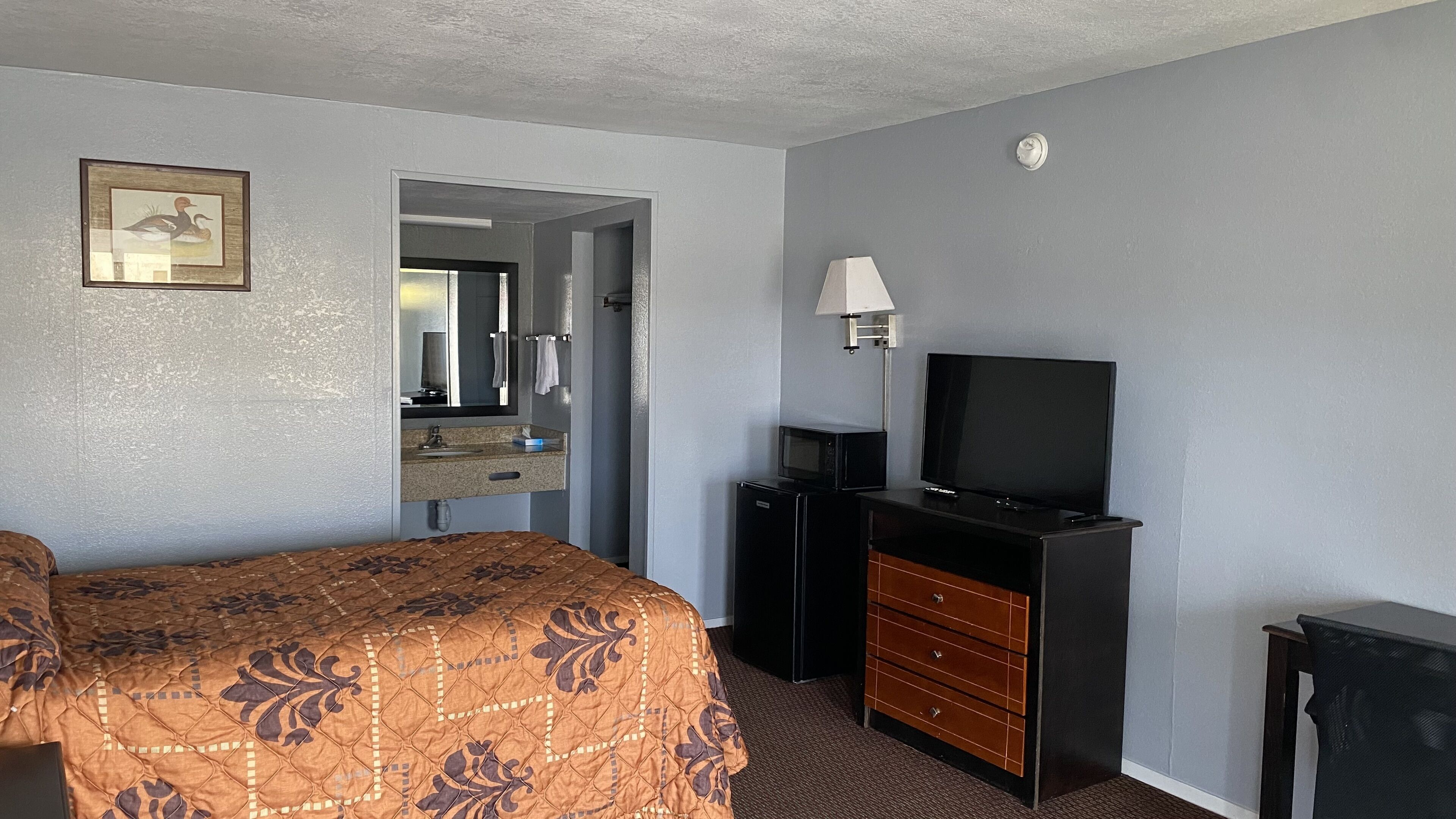 Una habitación de hotel con una cama, un tocador, un televisor y un espejo.