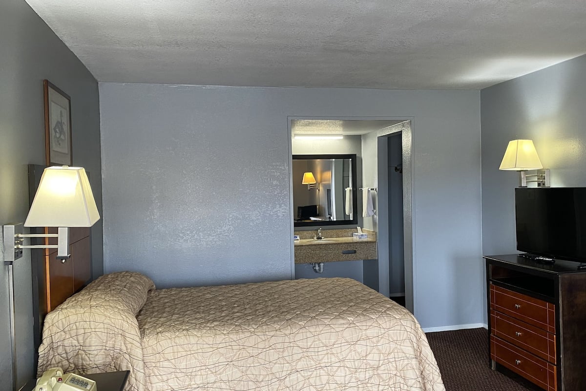 A hotel room with a bed, a dresser, a television, and a bathroom visible through an open door.