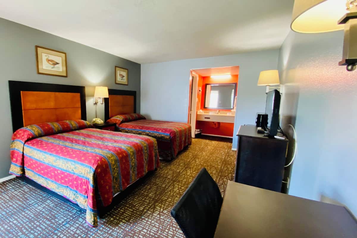 A hotel room with two beds, a desk, a chair, a desk lamp, a telephone, and a mirror.