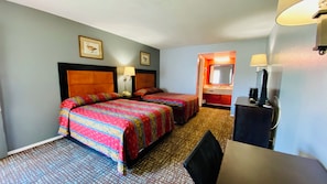 A hotel room with two beds, a desk, a chair, a desk lamp, a telephone, and a mirror.