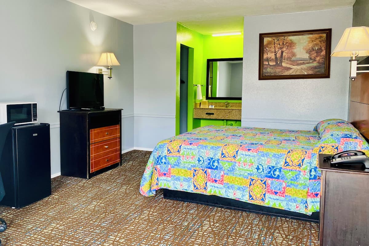 A hotel room with a bed, a desk with a computer, a television, a mirror, and a painting on the wall.