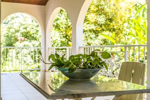 A glass table with a bowl of green plants in a covered outdoor area with white railings and a view of trees. - Les chambres d'hotes de la Villa Cayol (Fort-de-France)