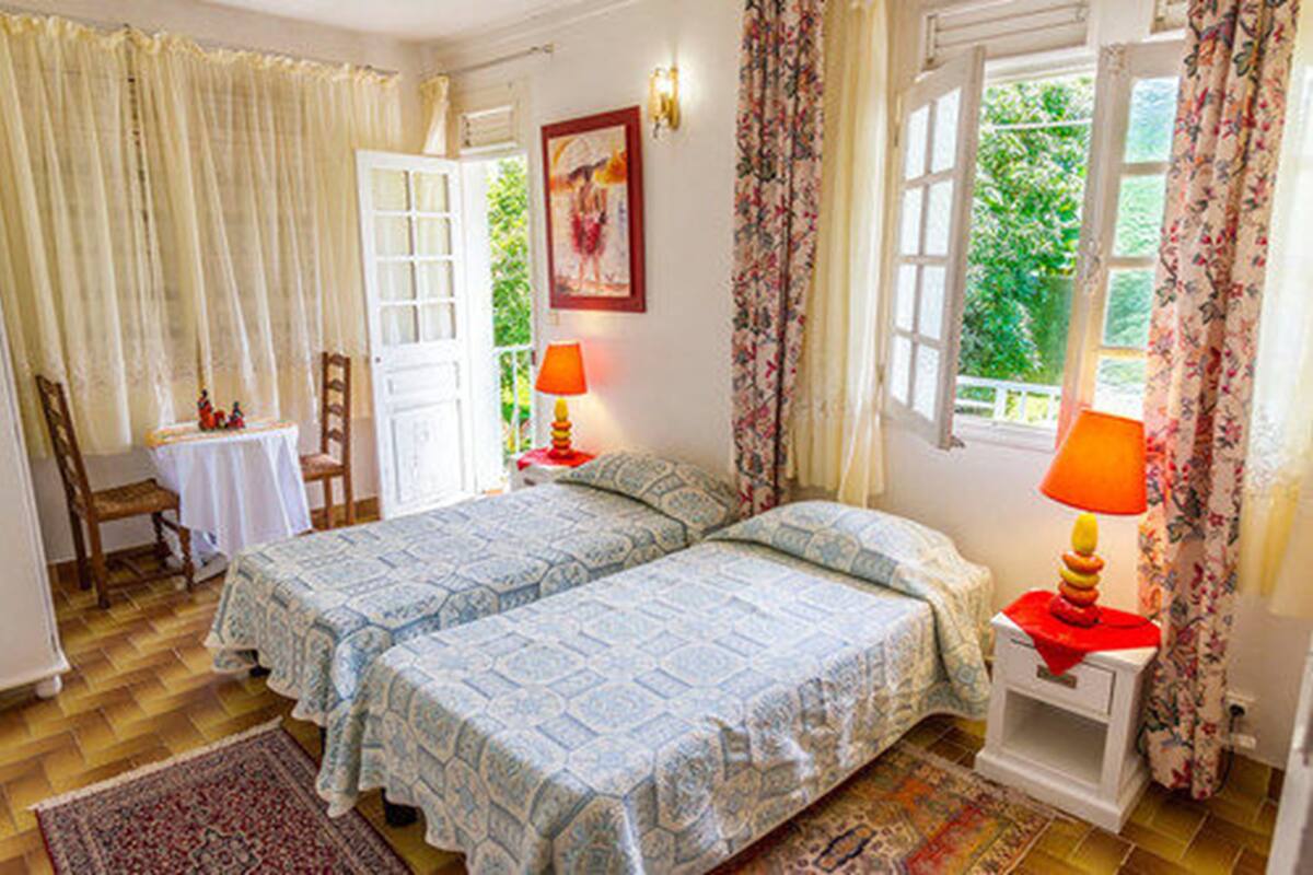 Ein Schlafzimmer mit zwei Betten, einem kleinen Tisch, einem Stuhl und einem Fenster mit Vorhängen.