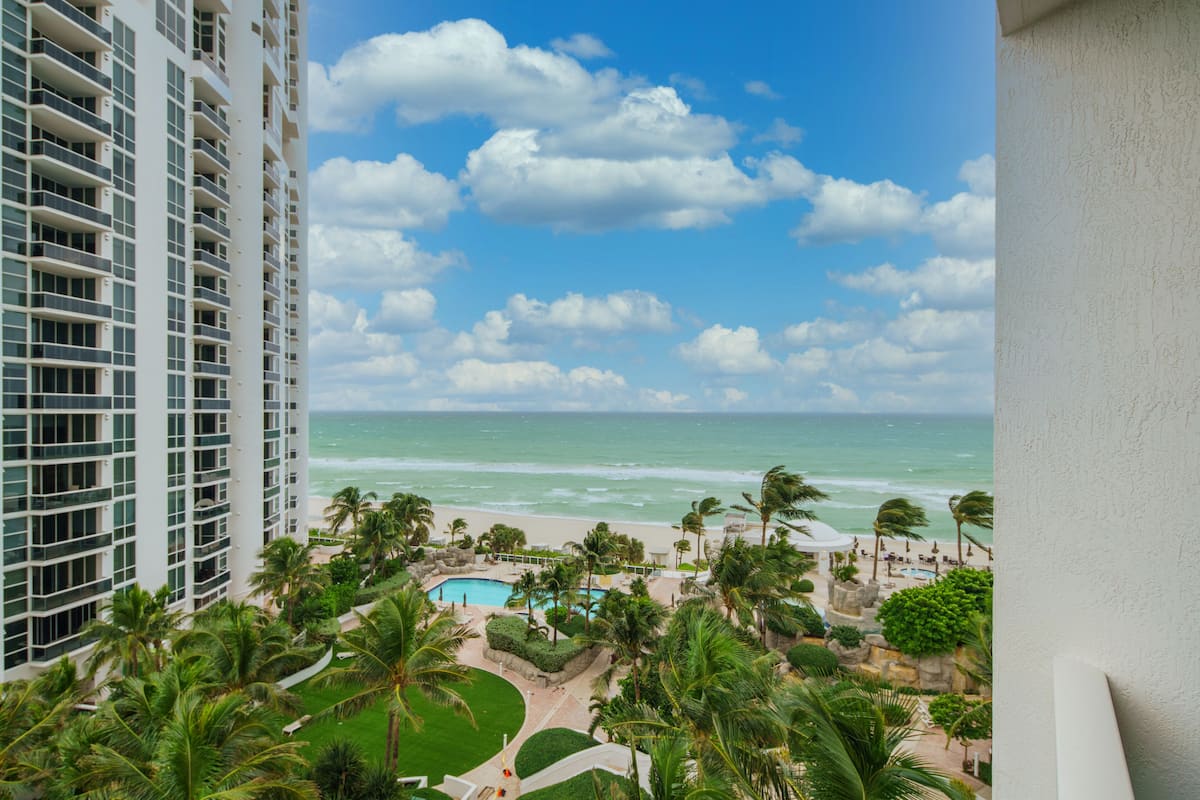 A high-rise hotel overlooking a beach with a pool and palm trees.