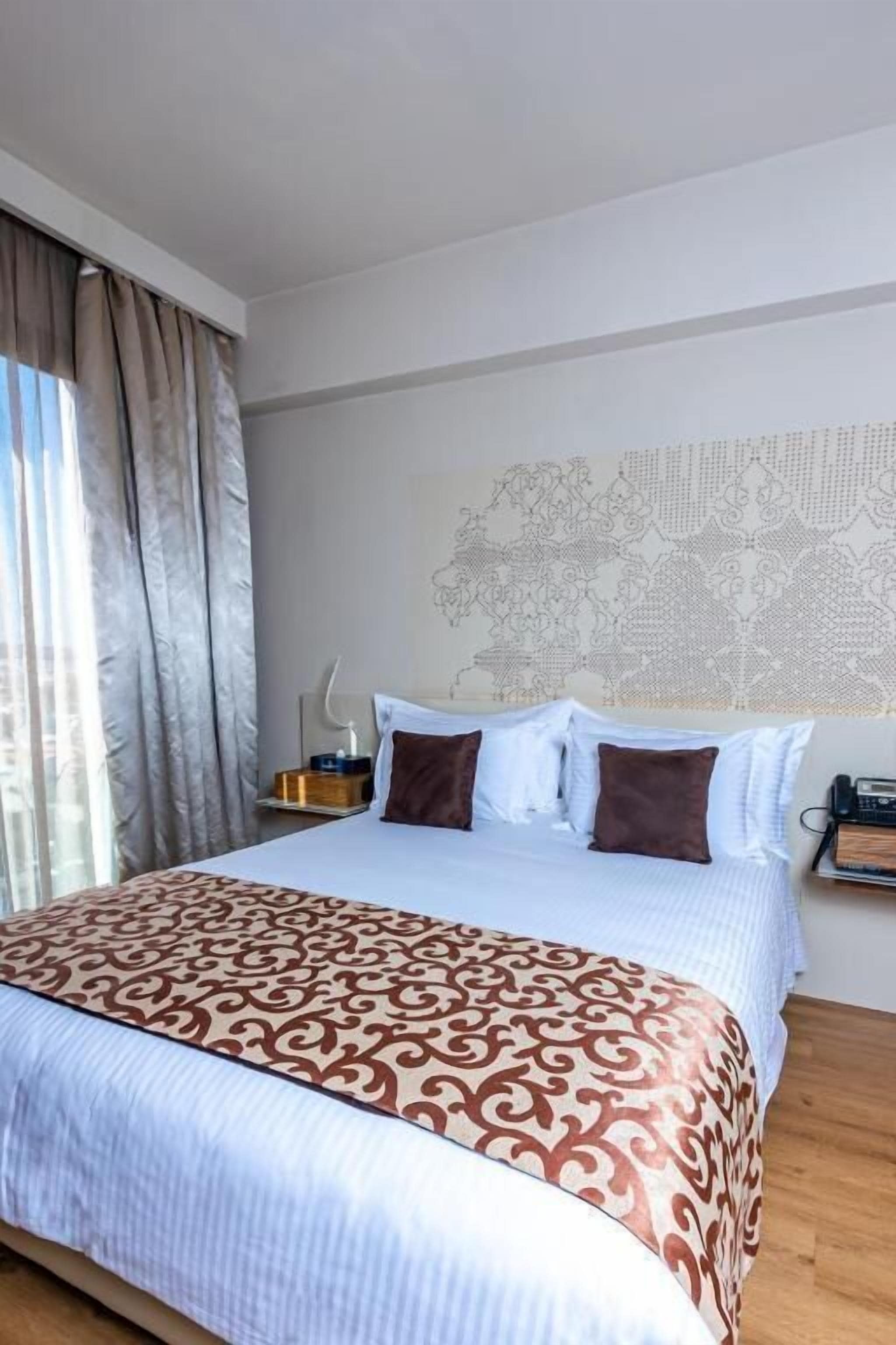 A hotel room with a large bed, a patterned bedspread, a world map on the wall, and a bedside table with a lamp.