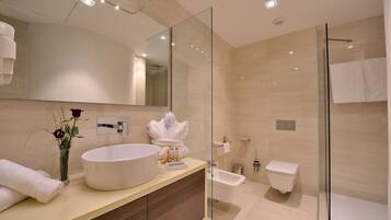 A modern bathroom with a large mirror, a round sink, a glass shower enclosure, and a toilet.