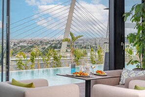 Une chambre d’hôtel moderne dotée d’une grande fenêtre donnant sur un paysage urbain et un pont. La chambre comprend une piscine, une table à manger avec un menu, et des sièges confortables.