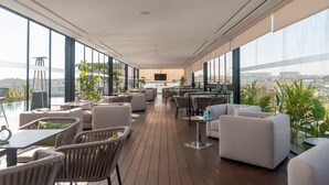 Ruime, open lounge met houten vloer, comfortabele zitplaatsen en grote ramen met uitzicht op de stad.
