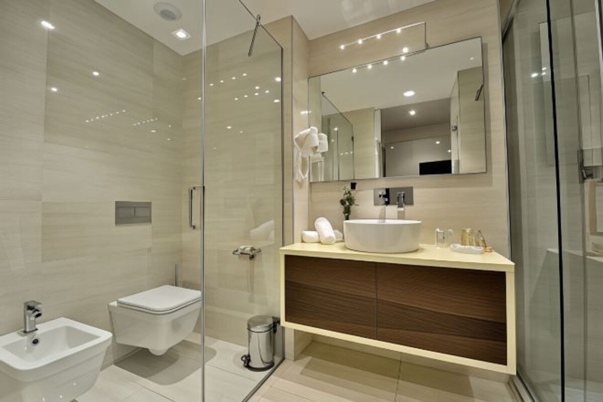 Een moderne badkamer met een douchecabine van glas, een wit toilet, een wastafel met spiegel en een badmeubel met een houten kastje.