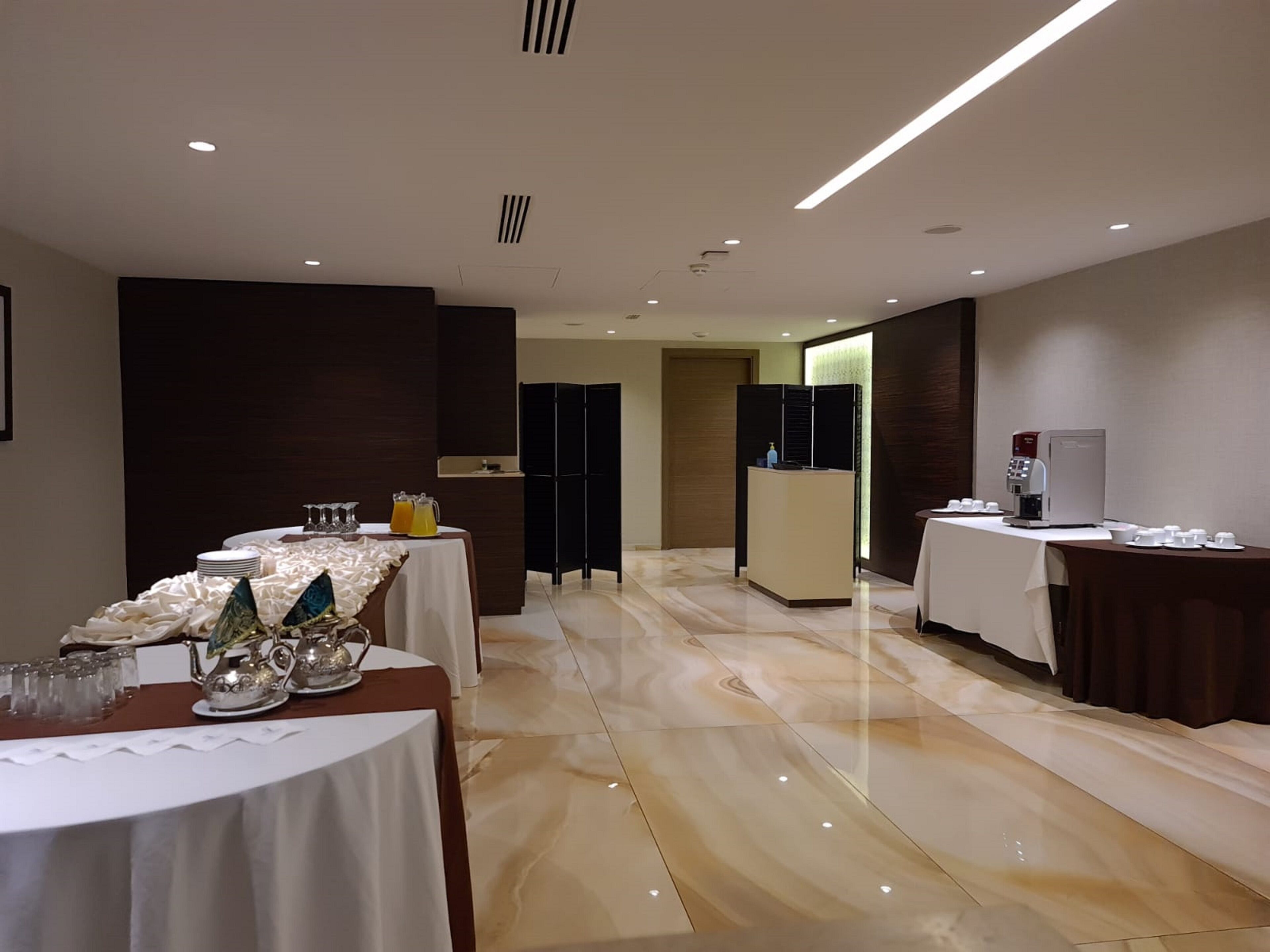 Un hall de hotel con una recepción, una mesa de buffet con comida y bebidas, y una estación de café.