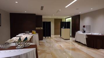 Un hall de hotel con una recepción, una mesa de buffet con comida y bebidas, y una estación de café.