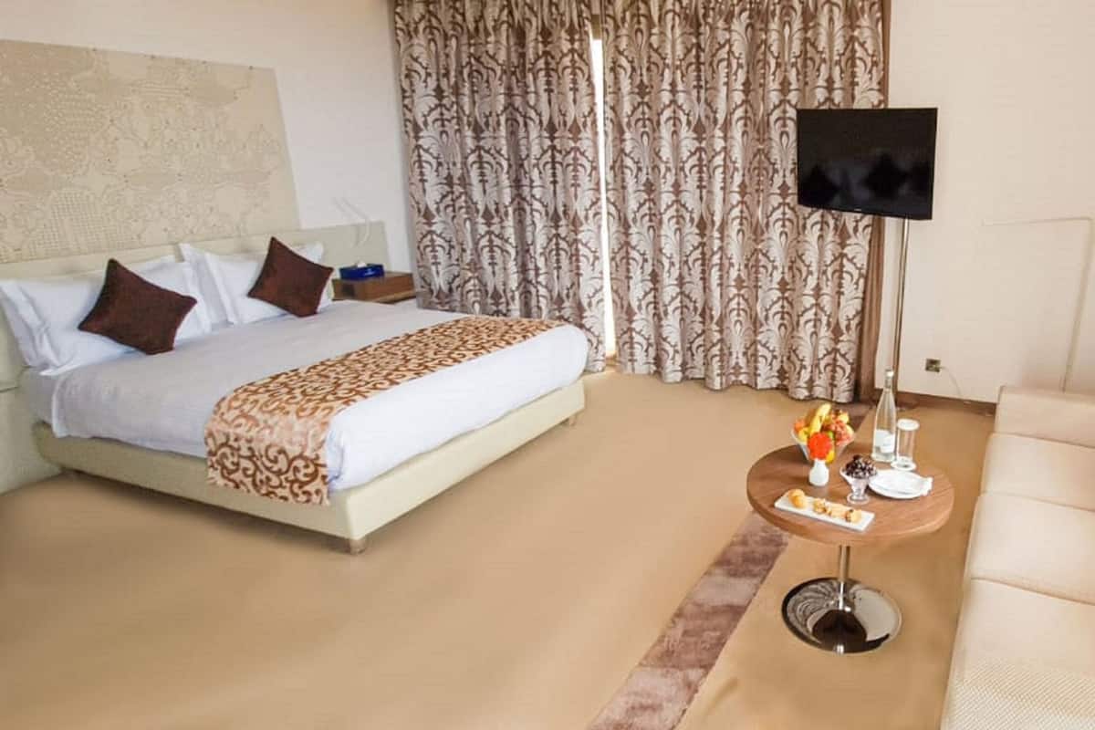 Ein Hotelzimmer mit Bett, Sofa, Fernseher und einem kleinen Tisch mit Blumenvase.