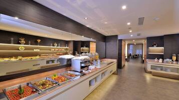 A modern hotel lobby with a buffet area featuring various food stations and a seating area in the background.