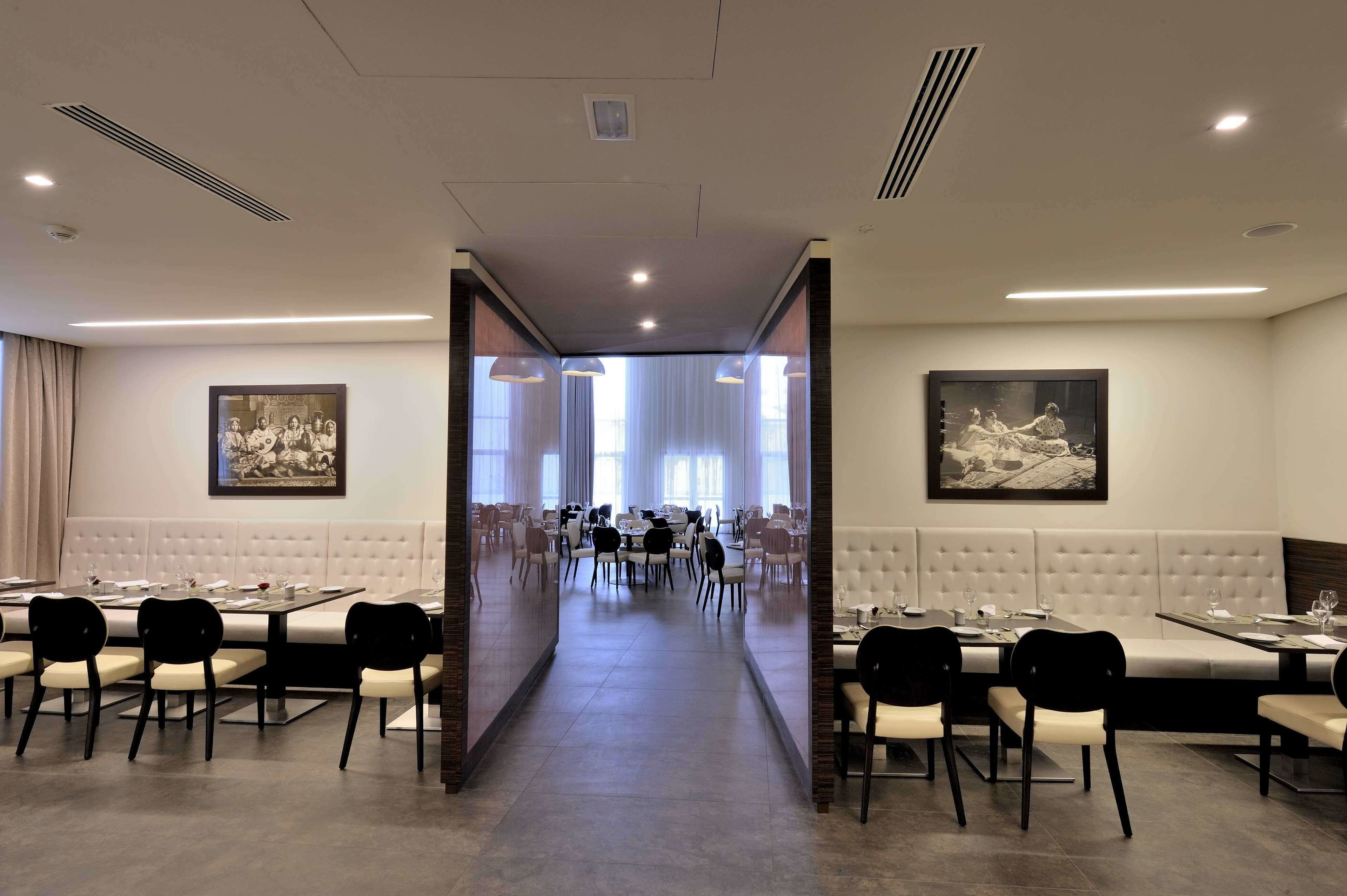 Un comedor de hotel con varias mesas y sillas, un pasillo central y cuadros en las paredes.