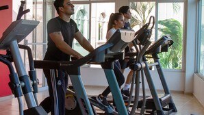 Ein Fitnessraum mit Ergometer und Laufbändern, großen Fenstern und Zimmerpflanzen.