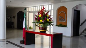 Ein Empfangsschalter mit Zimmerpflanze, einer Flagge und einem Schild für das Báez Paraíso Hotel in einer Lobby mit gefliestem Boden und einer Treppe.