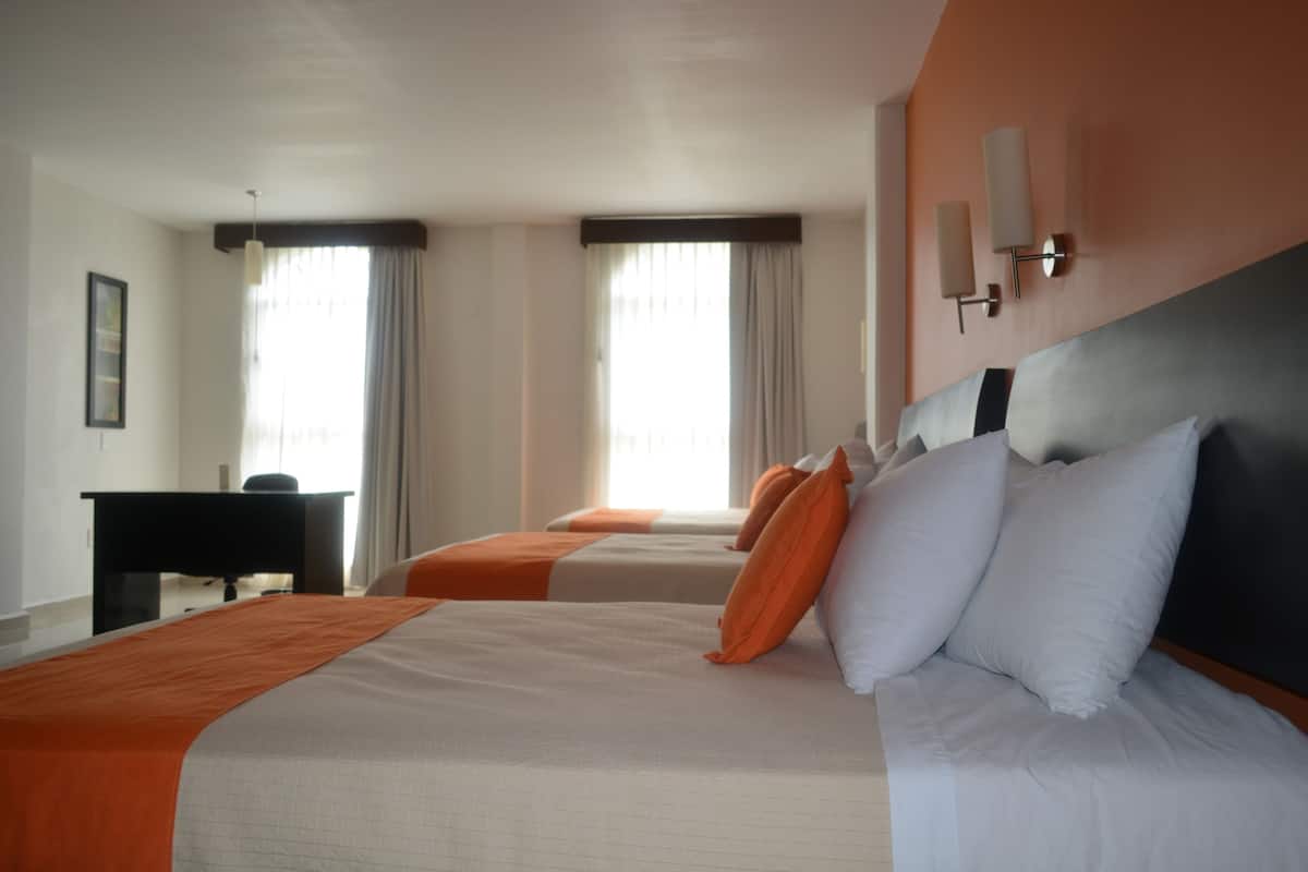 Ett hotellrum med två sängar, ett skrivbord och ett stort fönster med gardiner.